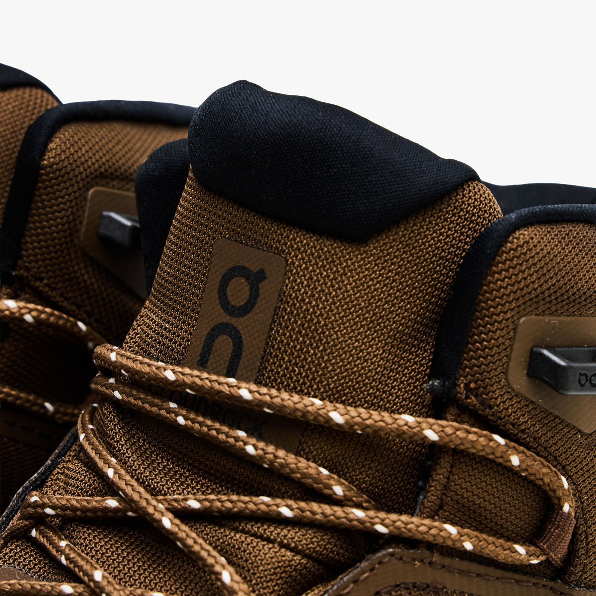 On Cloudrock Mid Waterproof. Close-up view showcasing earth brown mesh tongue, black On logo, metallic speed hooks, and multi-colored speckled laces.