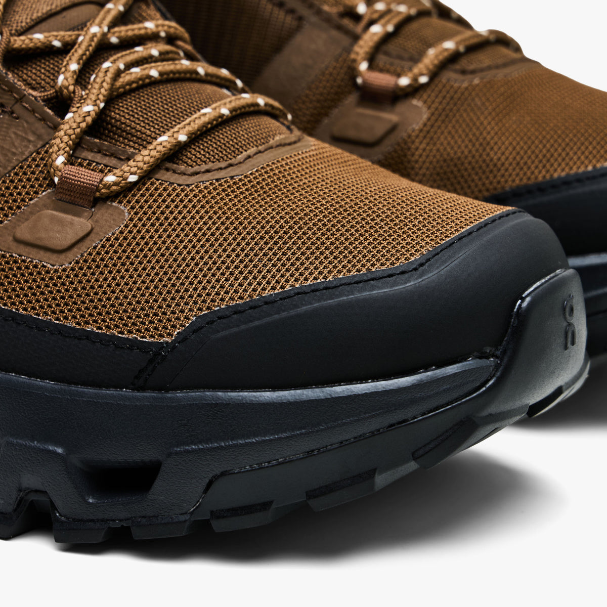 On Cloudrock Mid Waterproof. Close-up view highlighting reinforced black rubber toe cap, protective mudguard, and earth brown engineered mesh upper.