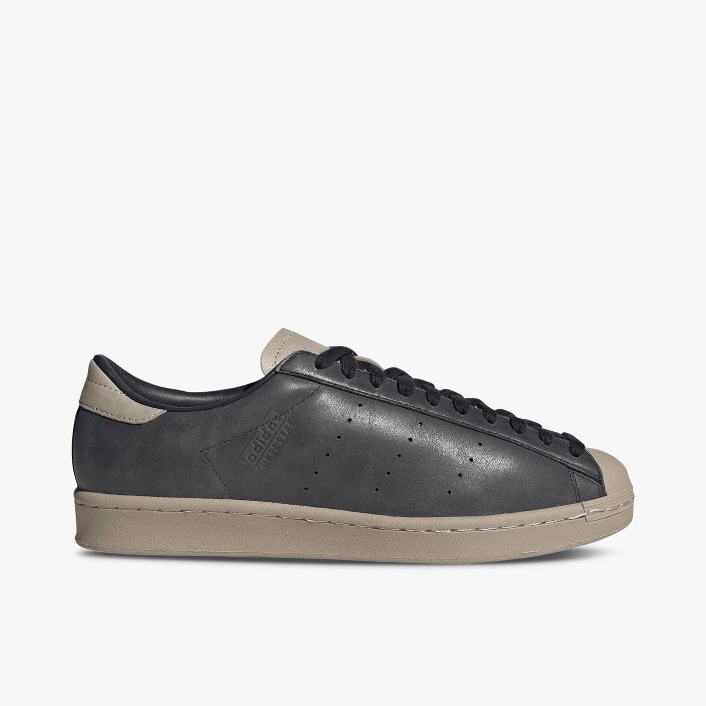 adidas Superstar Vintage Short Shell. Side view of Carbon leather sneakers with perforated three-stripes, adidas Superstar debossing on the sidewall, and Wonder Beige midsole.