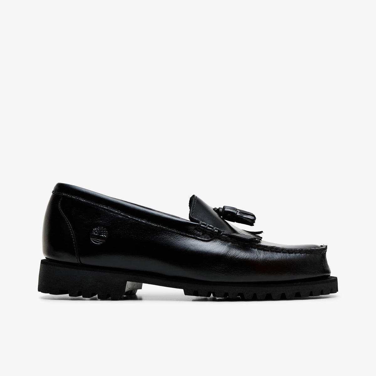 Timberland Authentic Loafer. Lateral profile view featuring polished black full-grain leather upper, kiltie fringe, double tassels, traditional moc-toe stitching, embossed Timberland tree logo on the heel, and rugged lug sole.