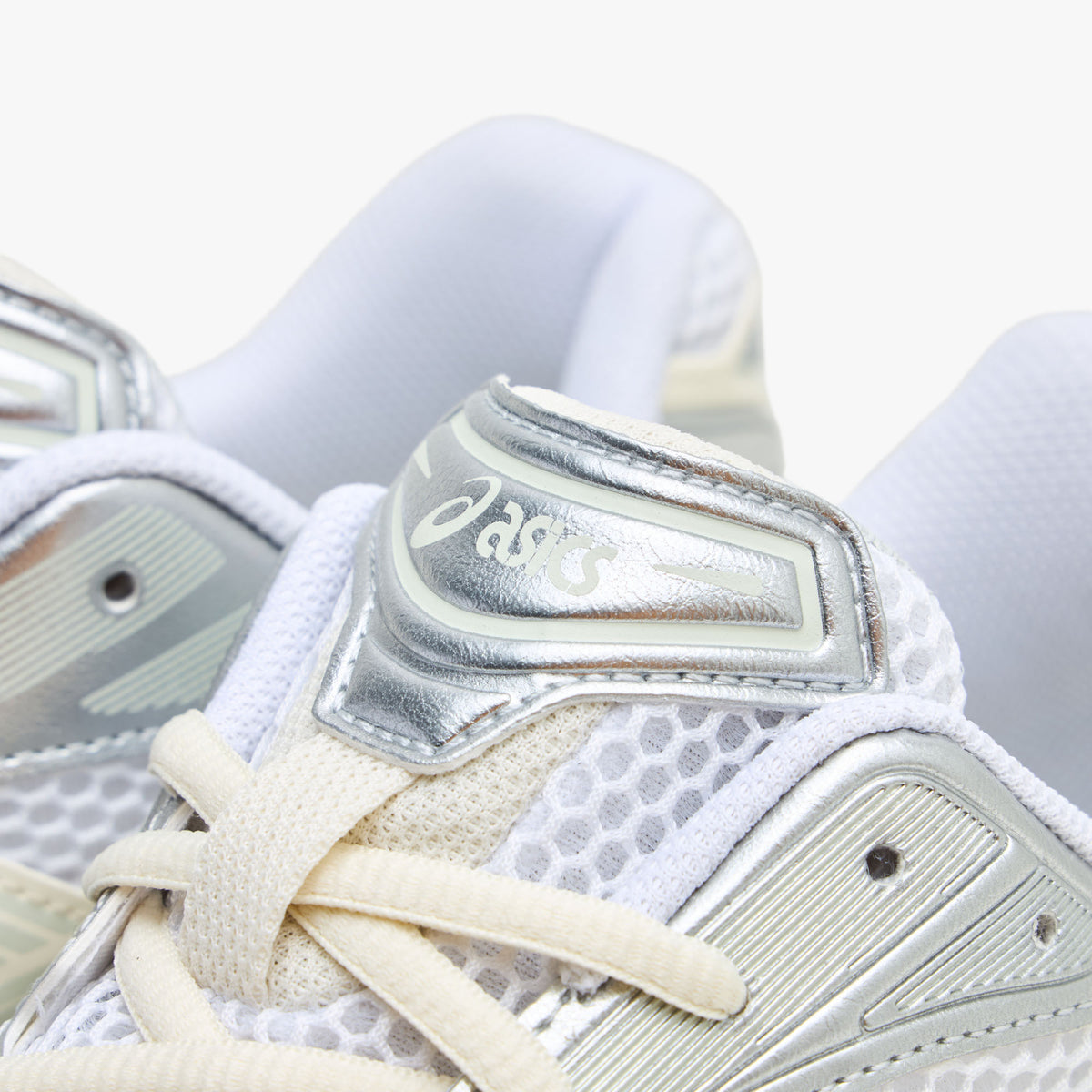 ASICS GEL-KAYANO 14. Close-up view of the tongue and collar region highlighting white open mesh, light sage eyestays, cream laces, and a metallic silver tongue badge with ASICS branding. 