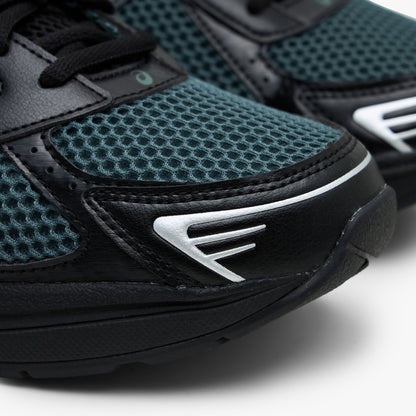 ASICS GEL-1130. Close-up view of the forefoot showing dusty fern green mesh toe box, black synthetic mudguard overlay, and silver metallic geometric toe accents. 