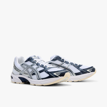 ASICS GEL-1130. Three-quarter view of a pair of running sneakers displaying white mesh uppers, dark midnight blue synthetic overlays, metallic silver Tiger Stripes, white laces, and off-white cushioned midsoles. 