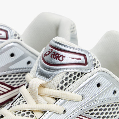 ASICS GEL-KAYANO 14. Close-up of silver overlay on mesh tongue showing red ASICS logo, silver synthetic overlays, and cream laces. 
