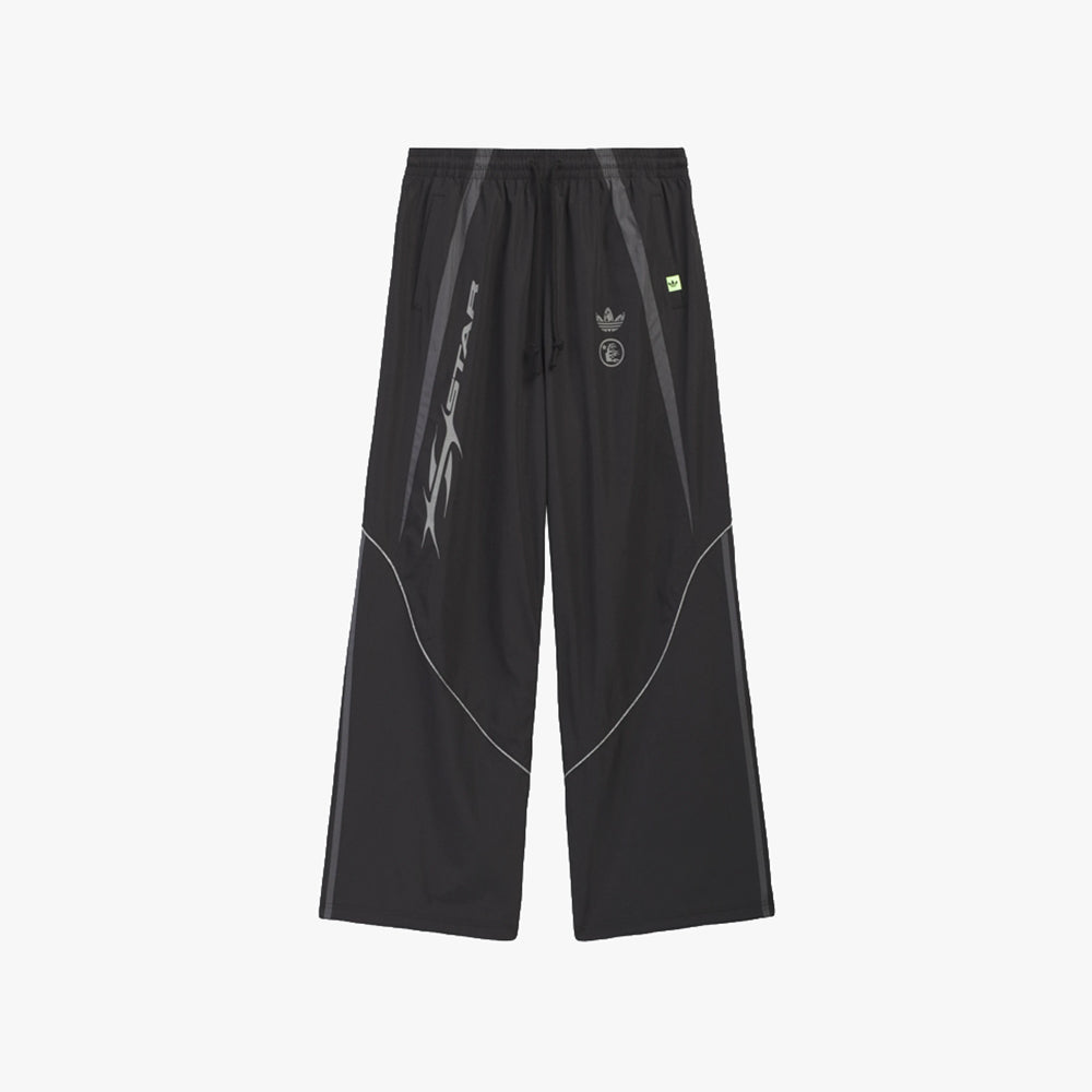 adidas Hellstar Ember Tracksuit Pants. Flat lay front view of black wide-leg track pants featuring an elastic drawstring waistband, contrast white piping along curved panel seams, vertical flame/script graphic printed along the right thigh, small grey adidas Trefoil and Hellstar emblem branding on the upper left thigh, neon yellow accent tab, and open-hem leg openings. 