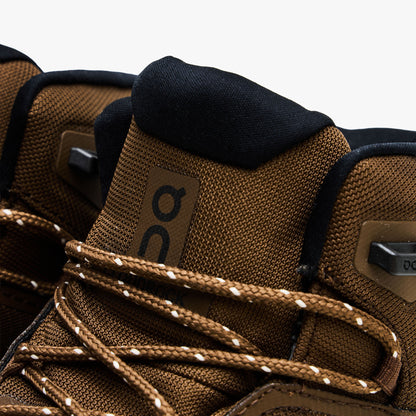 On Cloudrock Mid Waterproof. Close-up view showcasing earth brown mesh tongue, black On logo, metallic speed hooks, and multi-colored speckled laces. 