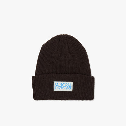 Balmoral Orchard Cotton Beanie. Front view of a dark coffee brown ribbed knit cotton beanie featuring a folded cuff and a white woven brand patch with bright blue "BALMORAL AUTOMNE - HIVER" text centered on the cuff. 