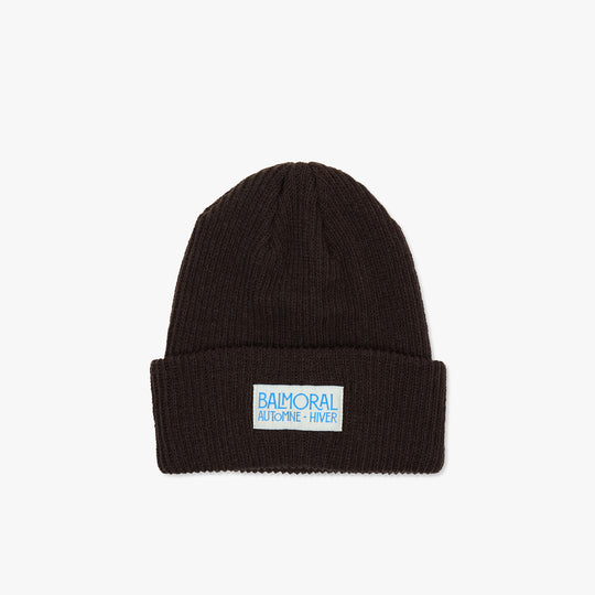 Balmoral Orchard Cotton Beanie. Front view of a dark coffee brown ribbed knit cotton beanie featuring a folded cuff and a white woven brand patch with bright blue "BALMORAL AUTOMNE - HIVER" text centered on the cuff. 