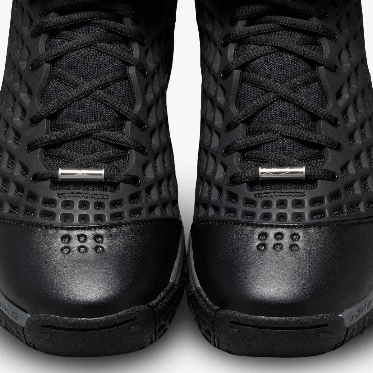 Nike Kobe III Protro. Close-up top-down view of both toe boxes showing smooth black synthetic leather toes, metallic silver lace dubraes, and diamond mesh net upper construction. 