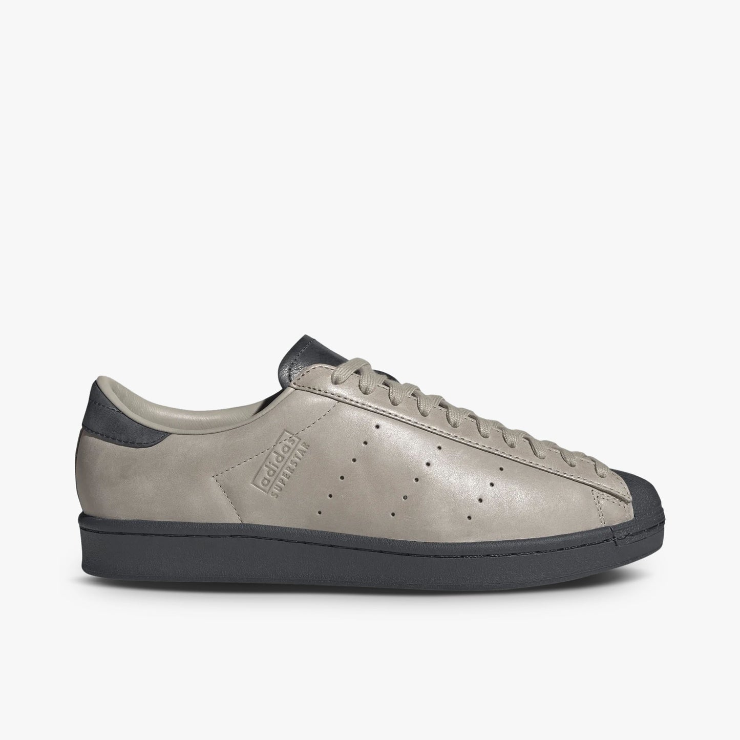 adidas Superstar Vintage Short Shell. Side view of Wonder Beige leather sneakers with perforated three-stripes, adidas Superstar debossing on the sidewall, and a Carbon midsole. 