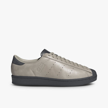 adidas Superstar Vintage Short Shell. Side view of Wonder Beige leather sneakers with perforated three-stripes, adidas Superstar debossing on the sidewall, and a Carbon midsole. 