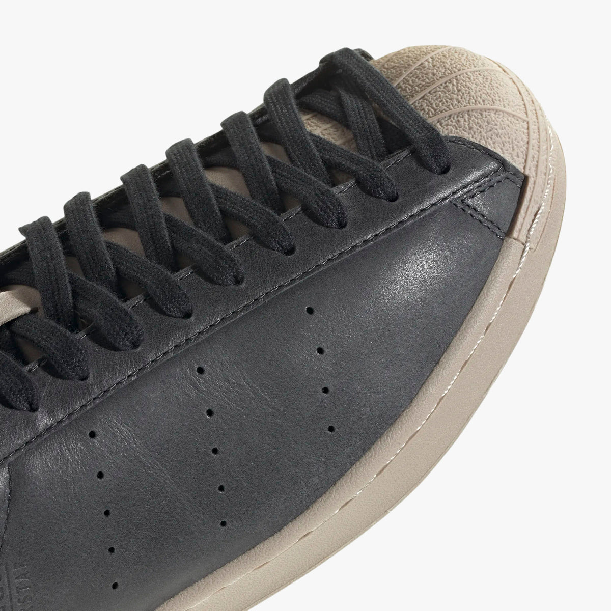 adidas Superstar Vintage Short Shell. Close-up of Wonder Beige rubber short shell toe, black laces, and perforated side ventilation holes. 
