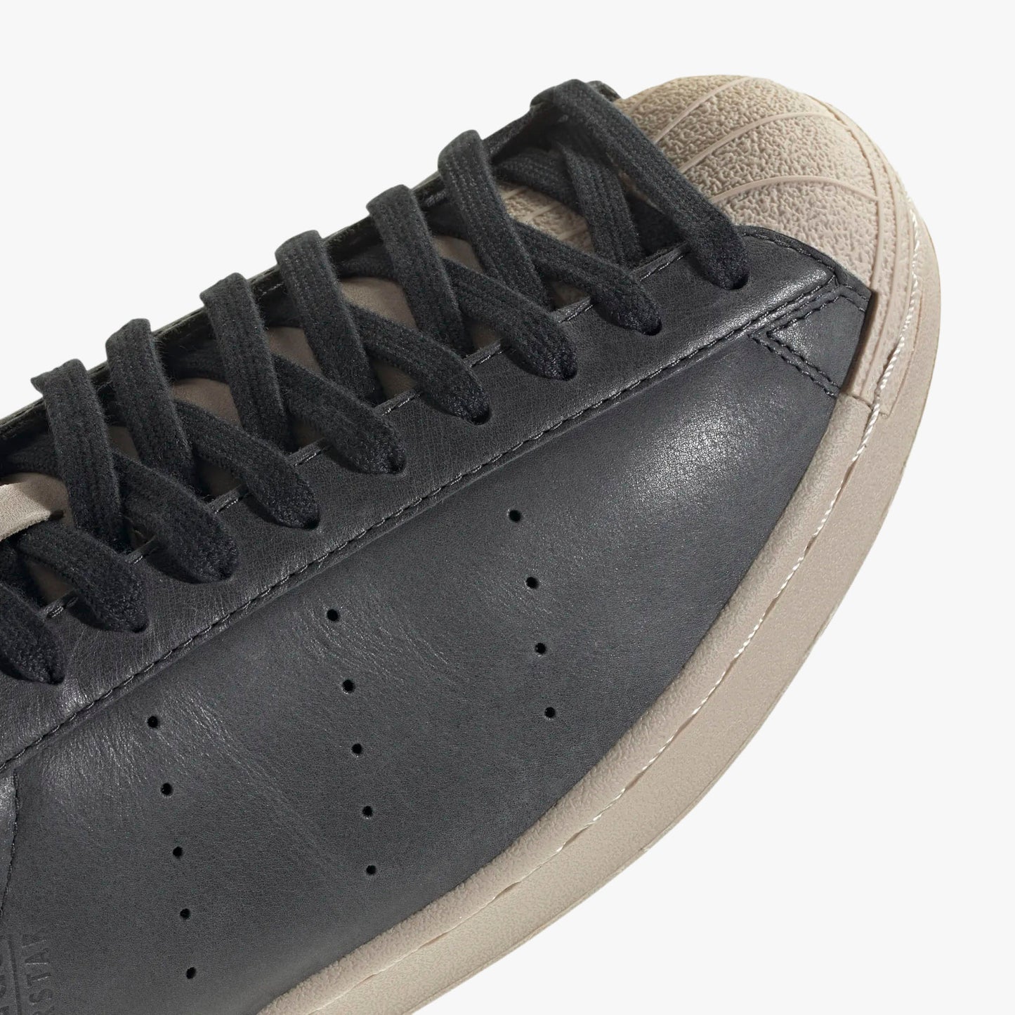 adidas Superstar Vintage Short Shell. Close-up of Wonder Beige rubber short shell toe, black laces, and perforated side ventilation holes. 