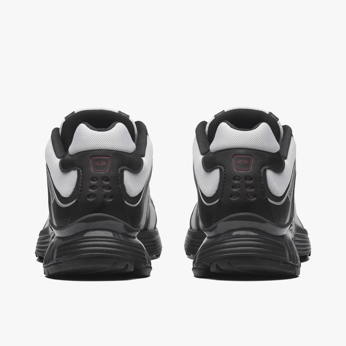 Salomon XT-WHISPER. Rear view of a pair of sneakers displaying black synthetic heel overlays, white collar trimming, red ACS heel insert badges, and black midsoles. 