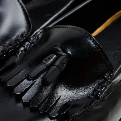 Timberland Authentic Loafer. Close-up view highlighting polished black full-grain leather vamp, kiltie trim, and decorative leather tassels. 
