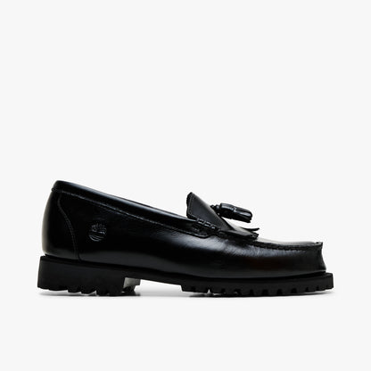 Timberland Authentic Loafer. Lateral profile view featuring polished black full-grain leather upper, kiltie fringe, double tassels, traditional moc-toe stitching, embossed Timberland tree logo on the heel, and rugged lug sole. 
