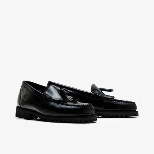 Timberland Authentic Loafer. Three-quarter view of pair showcasing shiny black full-grain leather construction, kiltie fringe and tassel detail, and thick lugged rubber soles. 