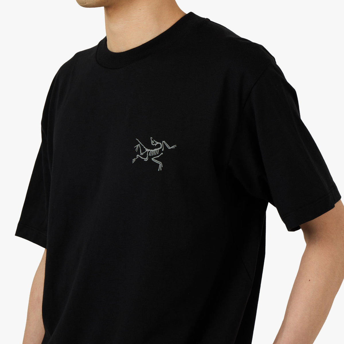 Arc'teryx Kragg SL Cotton T-Shirt. Close-up model view of left chest showing printed grey Arc'teryx Archaeopteryx bird logo and ribbed crewneck collar. 