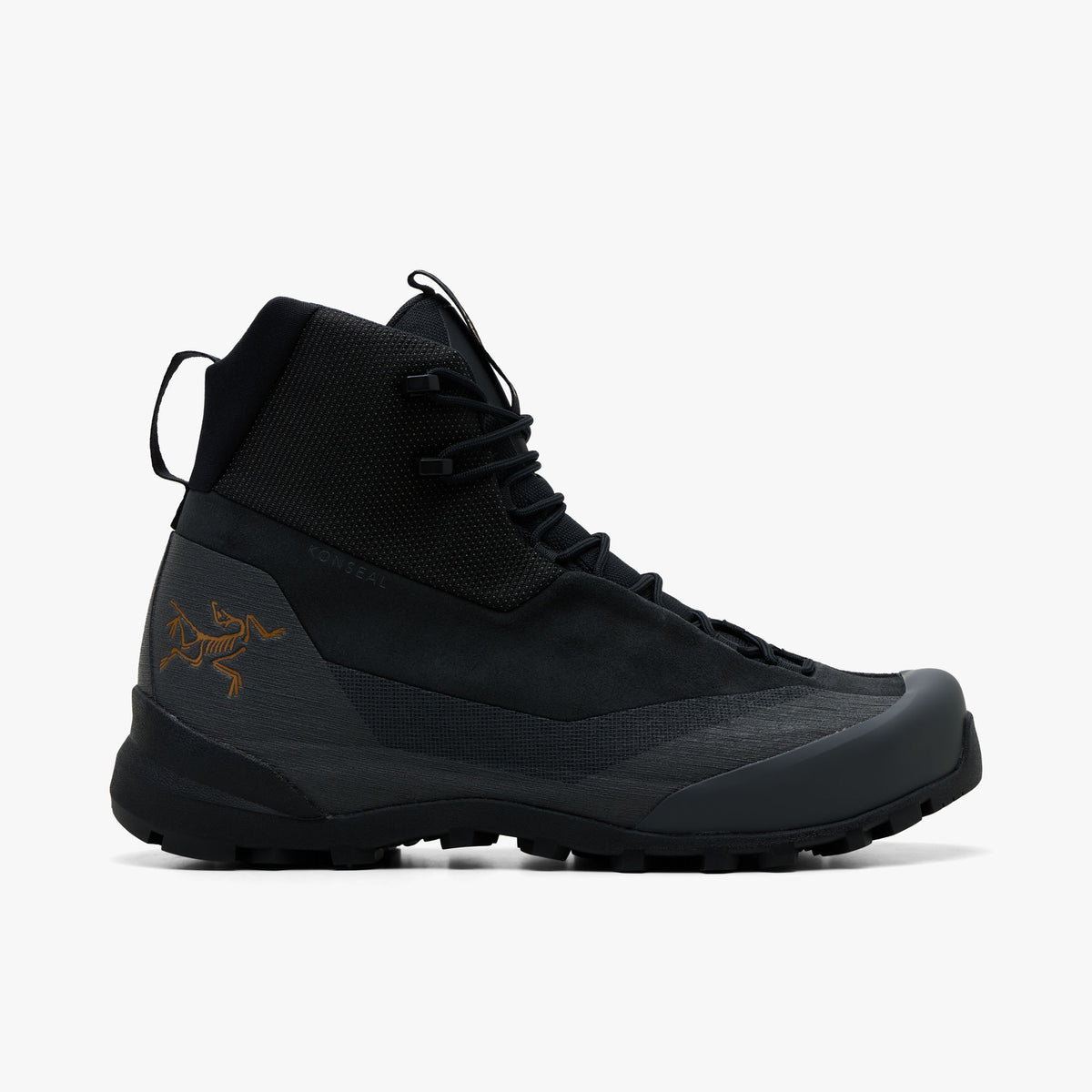 Arc'teryx Konseal Trek. Side view of mid-cut technical hiking boots featuring a black abrasion-resistant textile collar, nubuck upper, dark graphite TPU overlays, gold Archaeopteryx bird logo printed on the lateral heel, webbed lacing loops with speed hooks, and a lugged black Vibram outsole. 