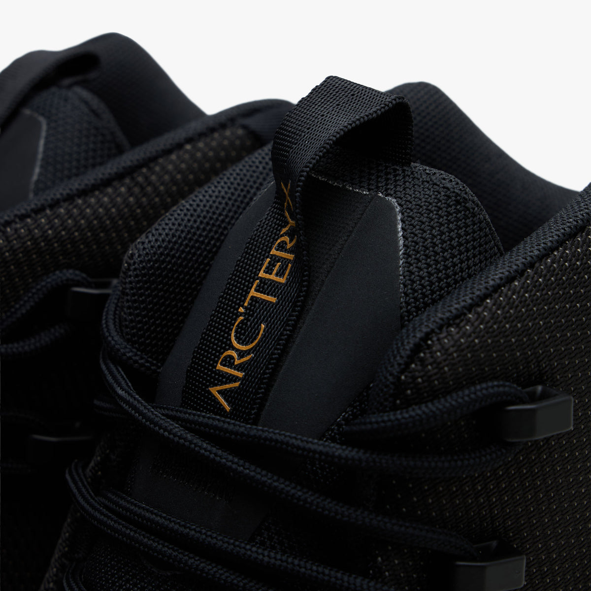 Arc'teryx Konseal Trek. Close-up view of the collar and tongue highlighting black lacing hardware, padded tongue pull tab with gold ARC'TERYX wordmark branding, and breathable mesh lining. 